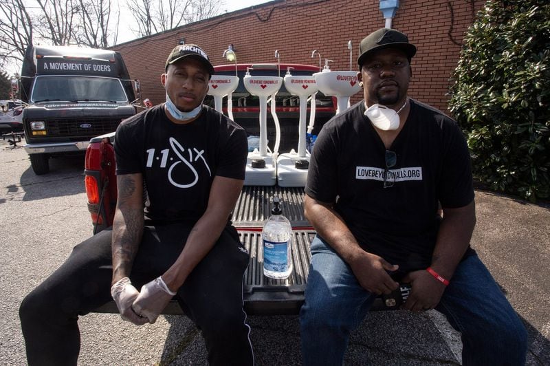 Grammy Award-winning hip-hop recording artist Lecrae (left) and Love Beyond Walls founder Terence Lester (right) sit on a truck bed filled with portable washing stations on Thursday, March 19, 2020, in College Park. The washing stations were distributed by Lecrae and volunteers with Love Beyond Walls, a nonprofit, throughout the Atlanta area in places with a high density of homeless people. AP PHOTO/ RON HARRIS