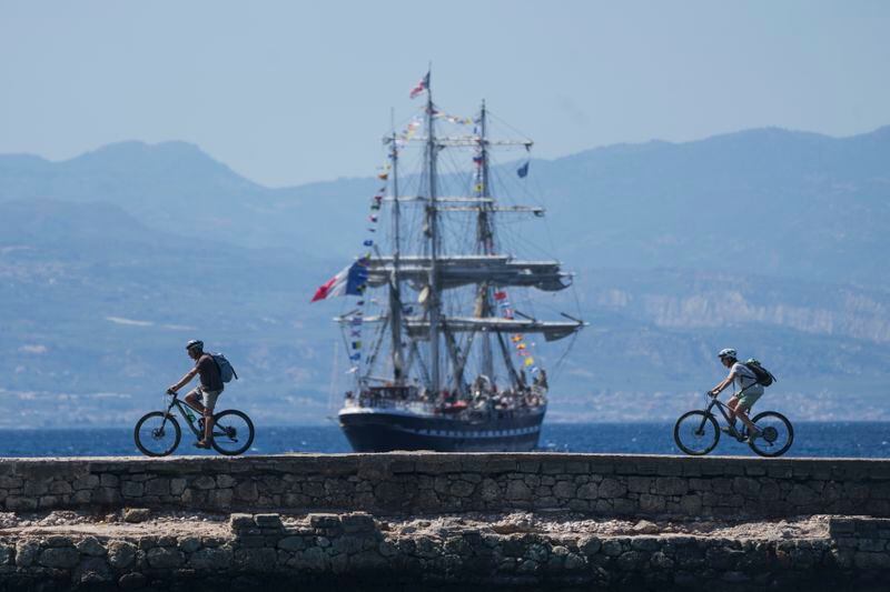FILE - Cyclists pass in front of the Belem, the three-masted sailing ship carrying the Olympic flame to France, as it sails near Corinth, Greece, April 28, 2024. The Olympic torch finally enters France when it reaches the southern seaport of Marseille on Wednesday May 8, 2024, on an armada from Greece. After leaving Marseille a vast relay route will be undertaken before the torch's odyssey ends on July 27 in Paris. (AP Photo/Petros Giannakouris, File)