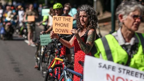 Kat Jones holds a sign during a rally on West Peachtree Street near 15th Street where William Alexander was hit and killed by a bus while riding on a scooter, Wednesday, July 24, 2019, in Atlanta. Organizers joined together as a "human protected sidewalk, bike and scooter lane" demanding the city prioritize protected bike and scooter lanes.  BRANDEN CAMP/SPECIAL