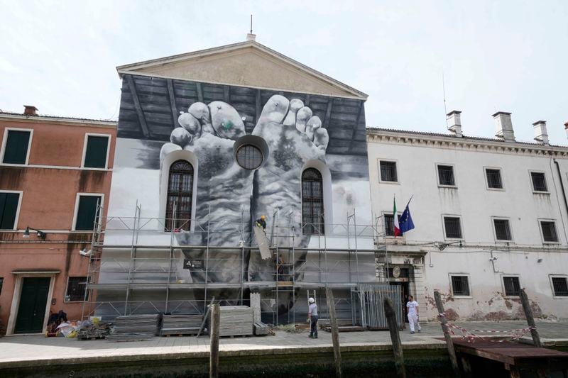 The installation 'I piedi, insieme al cuore, portano la stanchezza e il peso della vita" -'The feet, together with the heart, carry the tiredness and weight of life' by Italian artist Maurizio Catalan is displayed on the facade of the church next to the women's prison at the Giudecca island during the 60th Biennale of Arts exhibition in Venice, Italy, Wednesday, April 17, 2024. The Venice Biennale contemporary art exhibition opens Saturday for its six-month run through Nov. 26. The main show titled 'Stranieri Ovunque – Foreigners Everywhere' is curated for the first time by a Latin American, Brazilian Adrian Pedrosa. Pedrosa is putting a focus on underrepresented artists from the global south, along with gay and Indigenous artists. Alongside the main exhibition, 88 national pavilions fan out from the traditional venue in Venice's Giardini, to the Arsenale and other locations scattered throughout the lagoon city. (AP Photo/Luca Bruno)