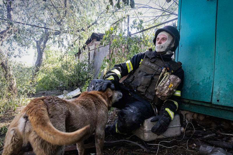 A firefighter pets a dog as he rests after putting out a fire in a private house hit by Russian shelling in Kharkiv, Ukraine, Friday, May 3, 2024. (AP Photo/Yevhen Titov)