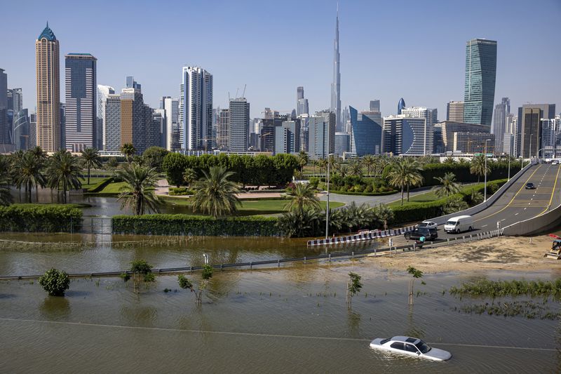 FILE - An abandoned vehicle stands in floodwater caused by heavy rain with the Burj Khalifa, the world's tallest building, seen in the background, in Dubai, United Arab Emirates, April 18, 2024. A new report says climate change played a role in the floods. (AP Photo/Christopher Pike, File)