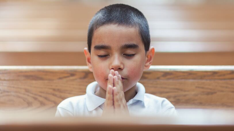 Schoolboy praying with eyes closed in empty church