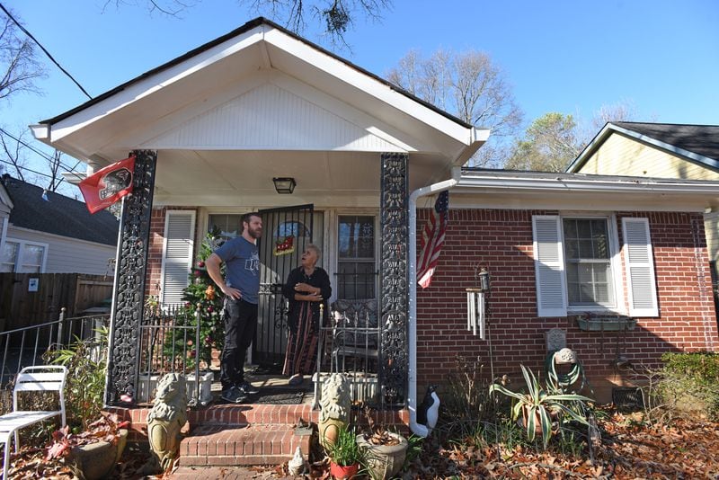 Justin Schaeffer and Annie Williams talk on her front porch where a neighborhood group, Kirkwood Cares, repaired and replaced gutters and roof. Schaeffer helps run the organization, with the goal of combating displacement in the community. (Hyosub Shin / Hyosub.Shin@ajc.com)