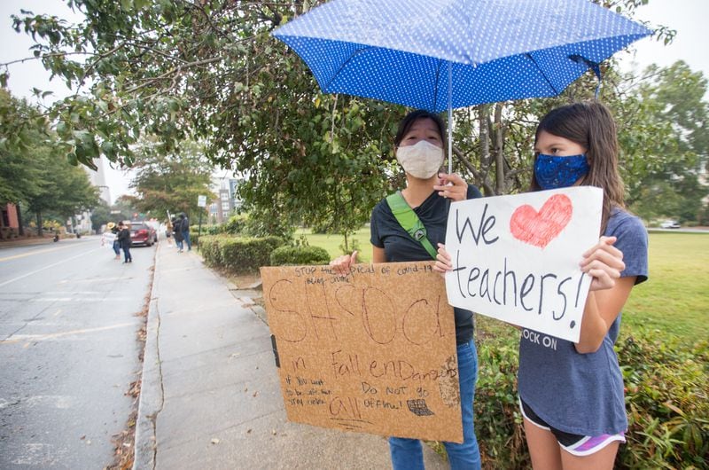 Teachers, parents and students, including Keri Chaya, left, and her daughter 10-year-old Calla Lockwood, right, protest in front of the Decatur City School Headquarters on Trinity Place in response to the district's plan to return teachers to schools in an effort to get back to in-person learning Friday, Oct, 9, 2020.  (Jenni Girtman for The Atlanta Journal-Constitution)