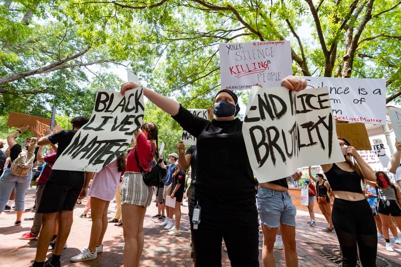 A protester holds two signs during a protest on the square over the recent Minneapolis police killing of George Floyd, held Wednesday, June 3, 2020, in Marietta, Ga. Social justice debates could be part of many holiday discussions this year, family therapists say. JOHN AMIS FOR THE ATLANTA JOURNAL-CONSTITUTION