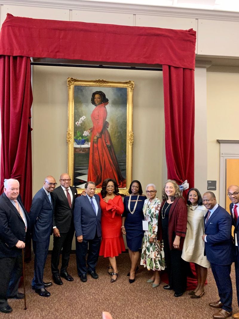 Oprah Winfrey, dressed in red, stands below a painting of her likeness at Morehouse College. Winfrey visited the Atlanta college Monday and announced she is donated $13 million toward a scholarship program she created 30 years ago. PHOTO CREDIT: MOREHOUSE COLLEGE.