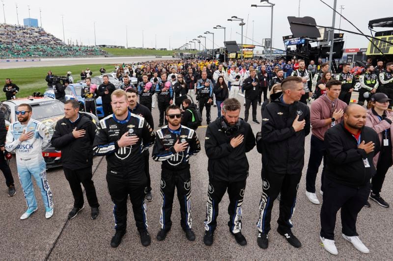 Ross Chastain, left, along with other drivers and crews stand along pit road during the playing of the National Anthem before a NASCAR Cup Series auto race at Kansas Speedway in Kansas City, Kan., Sunday, May 5, 2024. (AP Photo/Colin E. Braley)