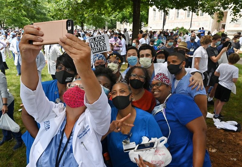 June 5, 2020 Decatur - Stephanie Drew, surgeon, DMD, holds her iPhone to take a selfie group photograph as Emory medical students, doctors, nurses and other health care staff gathered to take a knee for eight minutes and 46 seconds in memory of George Floyd "and countless others," in a demonstration they call White Coats for Black Lives at Emory University Quadrangle on Emory University campus in Decatur on Friday, June 5, 2020. Doctors these days are finding themselves at the intersection of America's race debate: giving advice to protestors on how to protect their eyes from tear gas and speaking their frustration at seeing people of color disproportionately sickened by COVID-19. On Friday at 1pm, a group organized by Emory med students is taking a knee at Emory University for eight minutes and 46 seconds in memory of George Floyd "and countless others," in a demonstration they call White Coats for Black Lives. (Hyosub Shin / Hyosub.Shin@ajc.com)