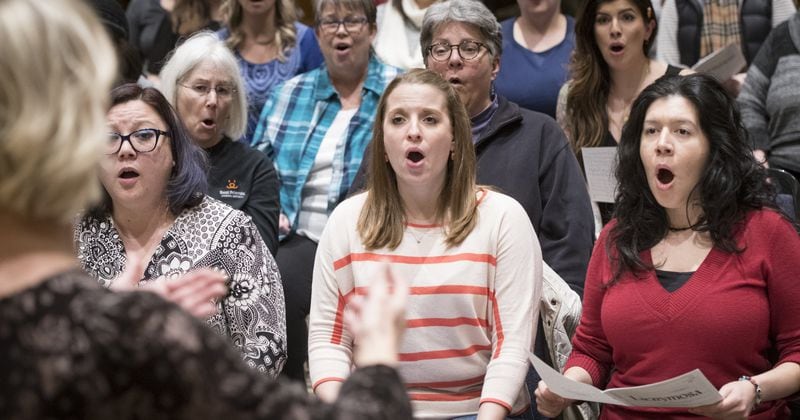Director Melissa Arasi (left, back to camera) leads the Atlanta Women’s Chorus as members including Ella Doyle (second from left), Amanda Rue (center) and Elisa Covarrubias (right) rehearse for the upcoming show “Rewind: The First Five Years.” JOHN AMIS / SPECIAL