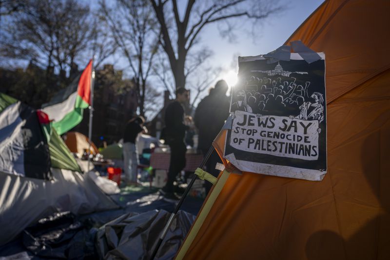 Students protesting against the war in Gaza stand next to a Palestinian flag and tents at an encampment in Harvard Yard, at Harvard University in Cambridge, Mass., on Thursday, April 25, 2024. (AP Photo/Ben Curtis)