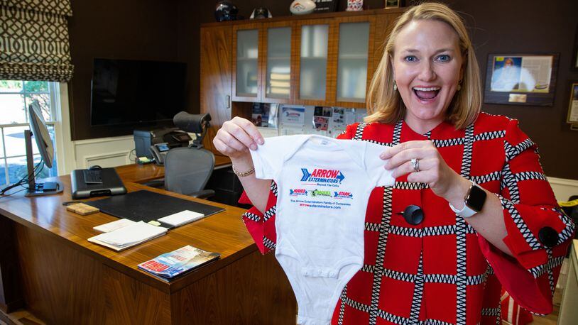Arrow Exterminators CEO and President, Emily Thomas Kendrick, holds up a baby onesie with the company logo on it at their National Headquarters in Atlanta. She started a tradition of giving one to every employee who had a new born baby.
