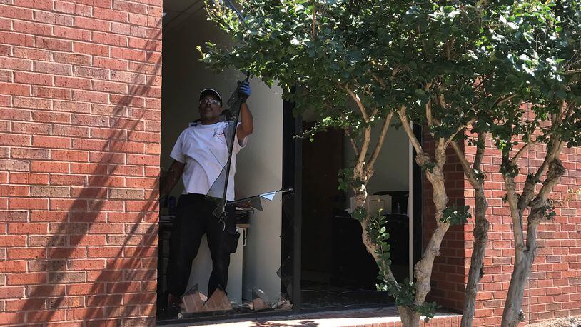A worker clears broken glass before boarding up a window at DeKalb County's Maloof Administrative Building. Vandals used rocks and possibly hammers and pick axes to break windows on Friday night. TIA MITCHELL/TIA.MITCHELL@AJC.COM