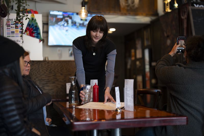 Allison Clarke, center, places menus down for customers as a patron at right takes a photo of a decorated basketball hoop at The Sports Bra sports bar on Thursday, April 25, 2024, in Portland, Ore. (AP Photo/Jenny Kane)