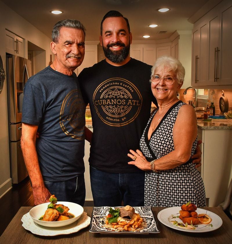 Osvaldo Llanes (father, from left), Ozzy Llanes (son) and Amarilys Llanes (mother) are shown with several Cuban dishes: (from left) Fricassee de Pollo con Papas (Chicken Fricassee with Potatoes), Palomilla Steak and French Fries, and Serrano Ham and Bechamel Croquetas. The photos were taken at the home of Ozzy Llanes, owner of Cubanos ATL. Food styling by Ozzy Llanes and Alex Valdivia / Chris Hunt/For The AJC