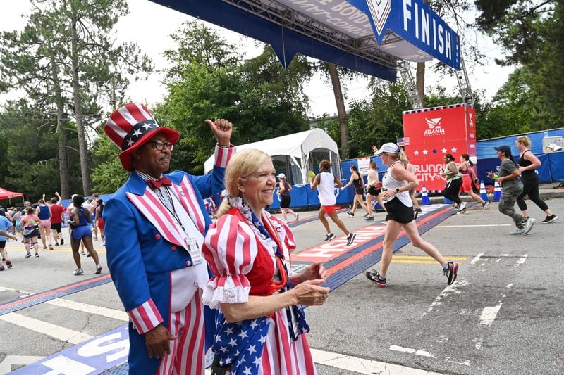 Reg and Paula Barnes are dressed as Uncle Sam and Betsy Ross cheer as runners cross the finish line of the 54th running of the Atlanta Journal-Constitution Peachtree Road Race on July 4, 2023, in Atlanta. (Hyosub Shin / Hyosub.Shin@ajc.com)
