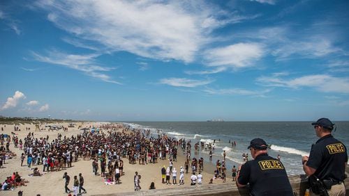Police officers watch a crowd of partiers gather on the beach for Orange Crush Saturday afternoon at Tybee Island. Police are investigating several incidents, including the attack of two women Sunday at the beach.