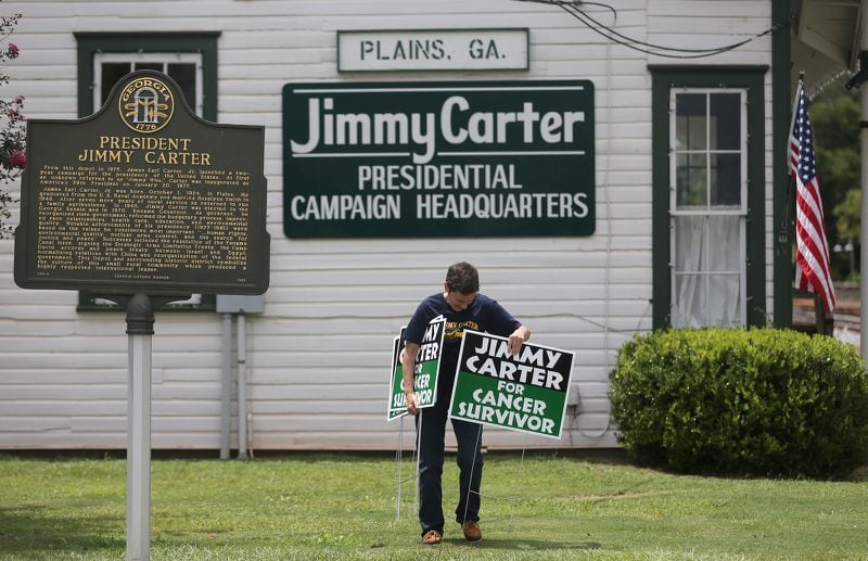 Jill Stuckey places "Jimmy Carter for Cancer Survivor" signs in downtown Plains in 2015. (Ben Gray / bgray@ajc.com)