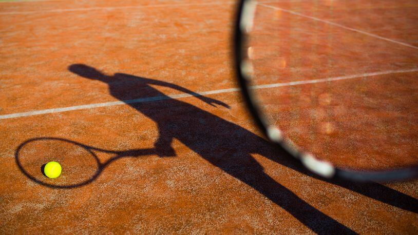Shadow of a tennis player in action on a tennis court (conceptual image with a tennis ball lying on the court and the shadow of the player positioned in a way he seems to be playing it)