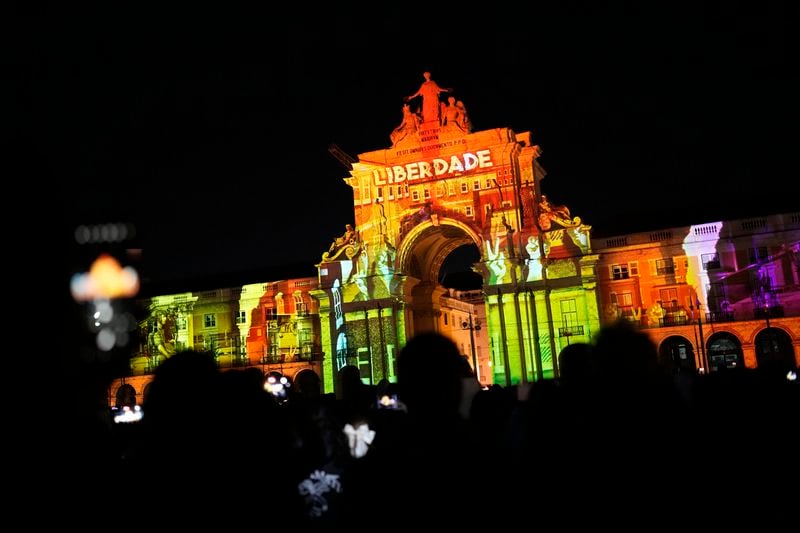 People use their cellphones to take pictures of a light show projecting the word Freedom on the arch of Lisbon's Comercio square, Wednesday, April 23, 2024, as the country celebrates the fiftieth anniversary of the Carnation Revolution. The April 25, 1974 revolution carried out by the army restored democracy in Portugal after 48 years of a fascist dictatorship. (AP Photo/Armando Franca)