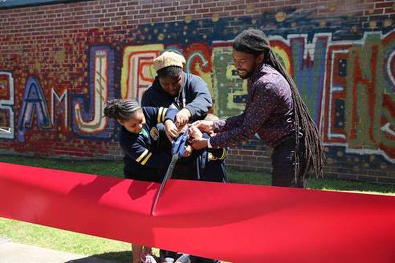 KIPP art teacher Eric Mack helps students (from left) Aryeon Johnson, Destiny Jackson and Emilio Velazquez cut the ribbon on the project. CONTRIBUTED BY CAROLYN SLOSS