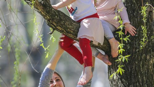 Nanny Emma Leabu hoisted Reagan Donnely, 3, (top left) and her sister, Ramsey Donnely, 2, onto a tree limb Thursday at the Duck Pond in Buckhead. JOHN SPINK / JSPINK@AJC.COM