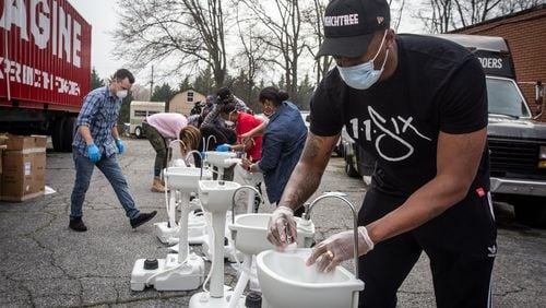 Hip-hop recording artist Lecrae assembles a portable washing station on Thursday, March 19, 2020, in College Park. Lecrae reached out to Love Beyond Walls, a nonprofit led by Terence Lester, to offer assistance, and he donated money for the first 15 washing stations, which are for the use of homeless people in the Atlanta area. AP PHOTO/ RON HARRIS