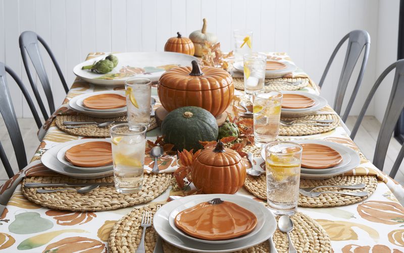 This fall-inspired tablescape features ceramic pumpkins from Crate and Barrel mixed in with real harvest vegetables. The Marin harvest tablecloth anchors the orange and green color-theme throughout.