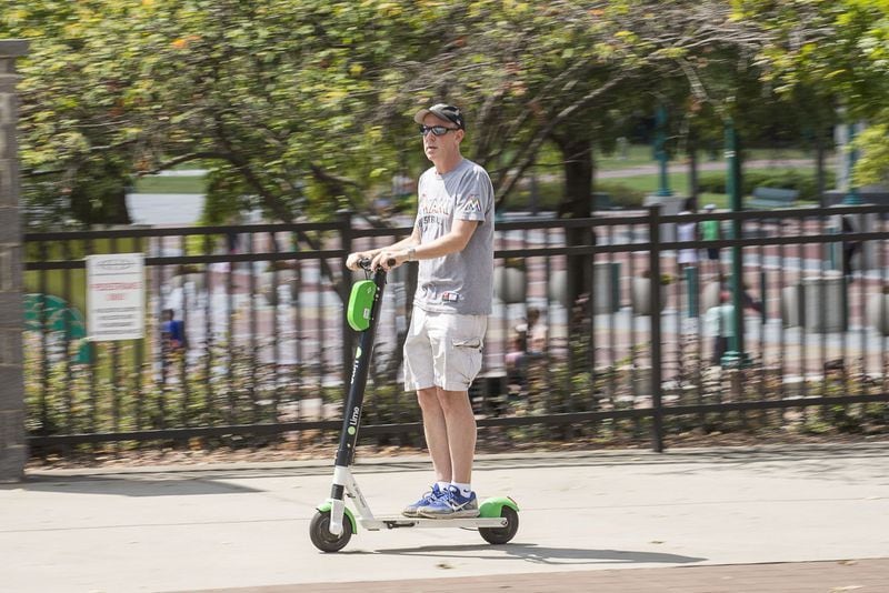 A man rides a shareable e-scooter in the bike lane along Centennial Olympic Park Drive NW.