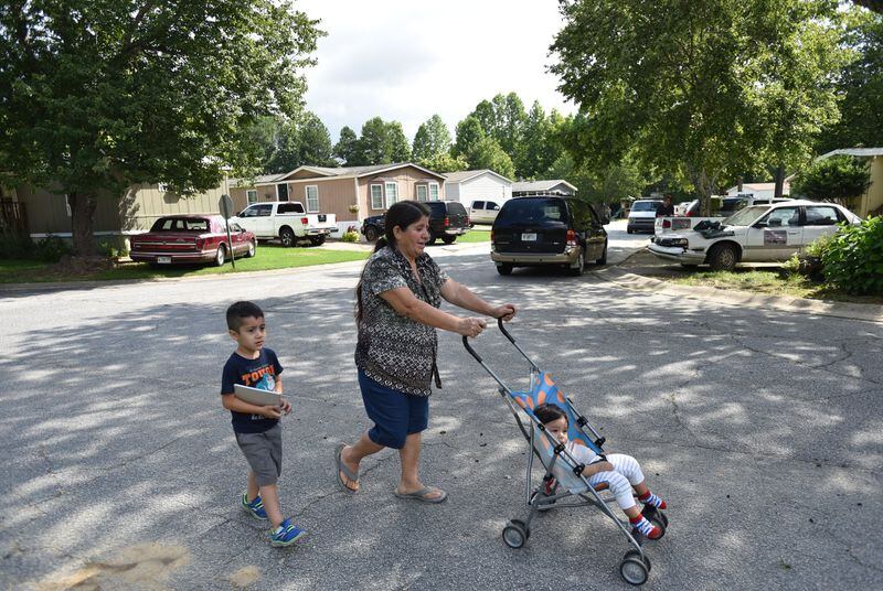 Etelvina Garcia walks with her grandchildren on Friday in the neighborhood where four children and their father were stabbed to death in Loganville. HYOSUB SHIN / HSHIN@AJC.COM