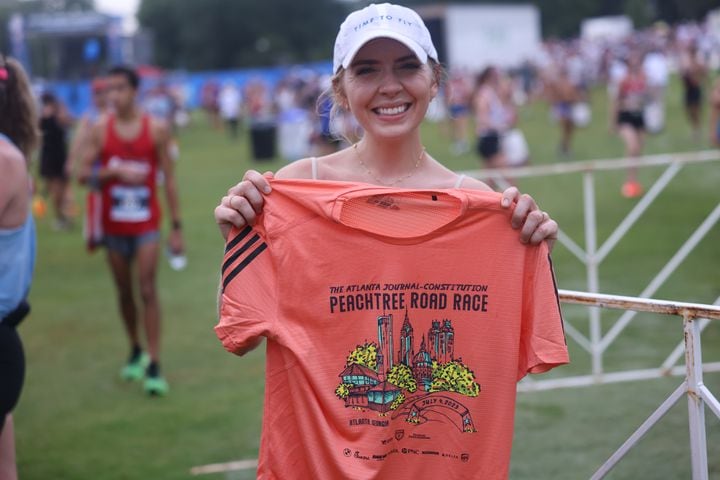 Lilly Meier of Clarkston holds up the winning T-shirt design after completing the 54th running of the Atlanta Journal-Constitution Peachtree Road Race in Atlanta on Tuesday, July 4, 2023.   (Jason Getz / Jason.Getz@ajc.com)