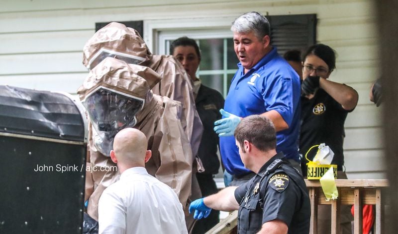 Investigators wearing hazmat suits exit a home in the 5400 block of Memphis Street in Forsyth County where a man and a woman were found dead Monday. JOHN SPINK / JSPINK@AJC.COM