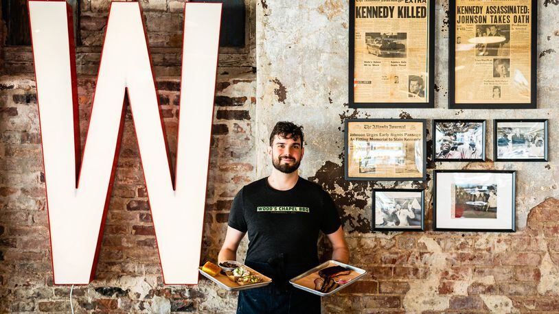 Server Zac Bodenhamer holds platters of barbecue and side dishes in front of a wall of political memorabilia at Wood’s Chapel BBQ. CONTRIBUTED BY HENRI HOLLIS