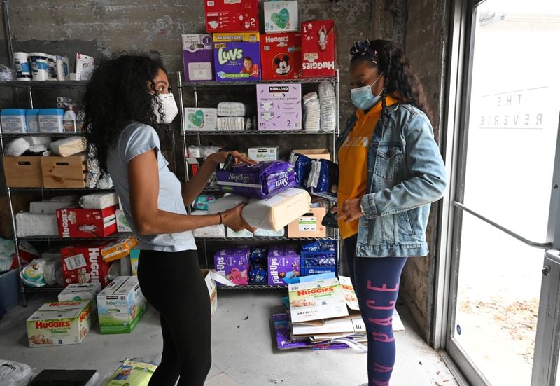 Jaycina Almond (left), founder of the Tender Foundation, hands items to volunteer Diana Owens, who will deliver them to a mother in need, at The Reverie, a co-working studio for women, in Atlanta on Saturday, Dec. 12, 2020. (Hyosub Shin / Hyosub.Shin@ajc.com)