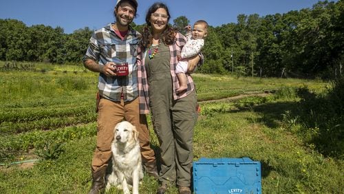 Levity Farms owners Zach and Ilana Richards pose for a photo with their 6-month-old daughter Harlyn and their dog Freedom at Levity Farms in Alpharetta. The couple is in the process of moving to a larger property in Madison. ALYSSA POINTER / ALYSSA.POINTER@AJC.COM