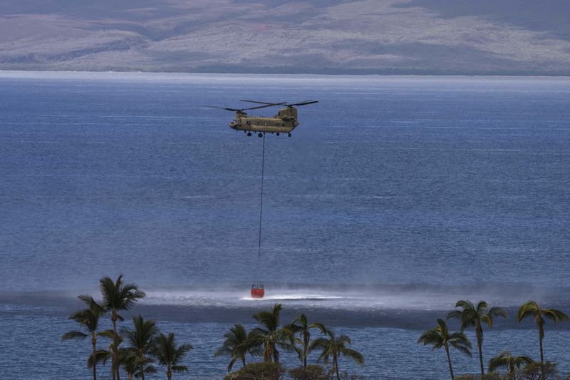 FILE - A Chinook helicopter scoops up water from the ocean near Lahaina, Hawaii, Wednesday, Aug. 16, 2023. The Maui Fire Department is expected to release a report Tuesday, April 16, 2024, detailing how the agency responded to a series of wildfires that burned on the island during a windstorm last August. (AP Photo/Jae C. Hong, File)