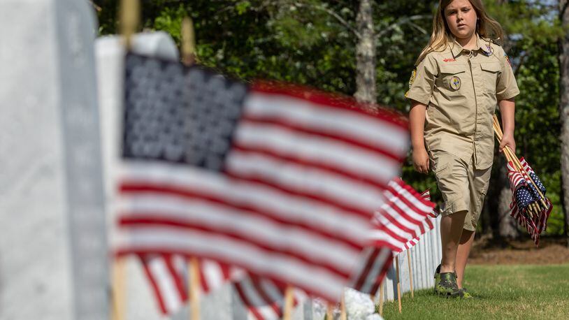 Karson Troville, with Troop 1755, places flags in front of tombstones at the Georgia National Cemetery in Canton Saturday, May 27, 2023. Volunteers will place an estimated 21,000 flags on tombstones during the ceremony (Steve Schaefer/steve.schaefer@ajc.com)
