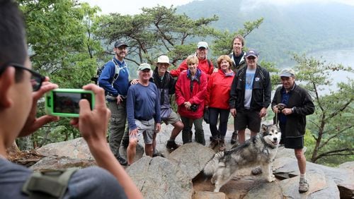 May 21, 2015, Harpers Ferry, WV: The Appalachian Adventure reunion crew enlists a hiker to help with a group photo at Weverton Cliff above Harpers Ferry, WV. Pictured are Chris Hunt, from left, Steve Grant, Scott Huler, Robin Rombach, Don Hopey, Martha Ezzard, Bo Emerson, John Ezzard and Walter Cumming with his dog Tanook. Ben Gray / bgray@ajc.com