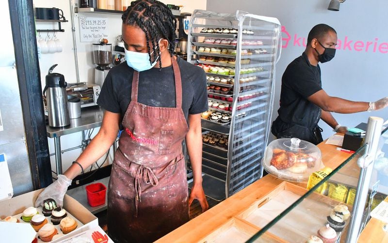 Seanba Anderson (left), kitchen manager at Kupcakerie, fulfills delivery orders of fresh-made cupcakes while co-owner Henry Adeleye takes care of morning duties at the front counter of the bakery in downtown East Point. CONTRIBUTED BY CHRIS HUNT PHOTOGRAPHY