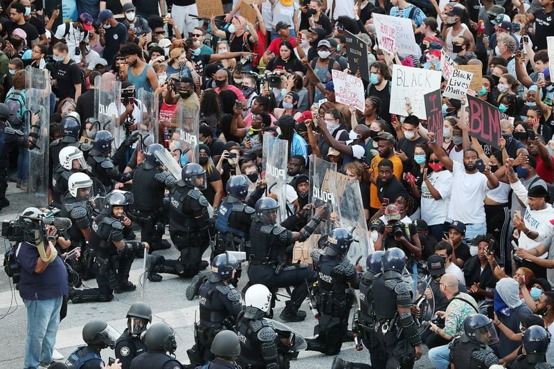 In a show of peace and solidarity, law enforcement officials with riot shields take a knee before protesters during a fourth day of protests on Monday, June 1, 2020, in Atlanta. 