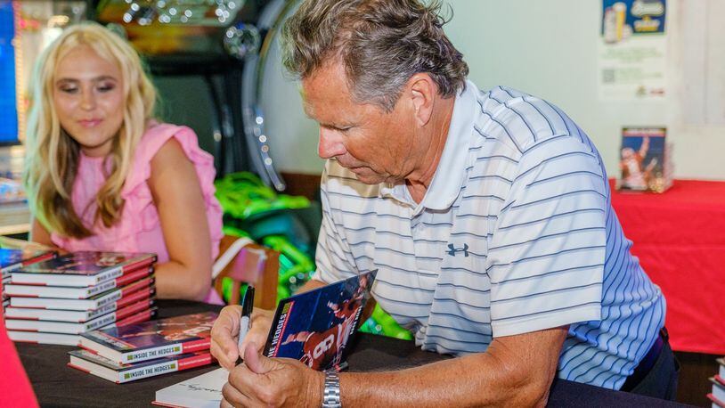 Buck Belue, quarterback of Georgia’s 1980 national championship team, signs a copy of his new book Inside the Hedges at Coach’s Corner in Savannah on July 8, 2022, as daughter Audrey looks on. Photo by Chris McShane (provided by Buck Belue).