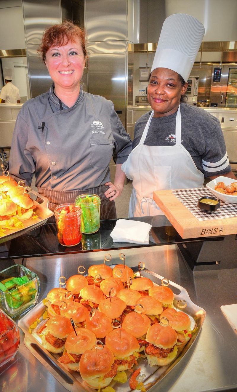 Chef Juliet Peters (left) and Carrichia Clark of the West Nest, which is operated by local nonprofit Westside Works, stand in front of the hand-breaded free-range fried chicken sandwiches they helped prepare at Mercedes-Benz Stadium. A portion of the proceeds from the West Nest concession in Section 324 will benefit the Westside Works Culinary Arts program, a six-week intensive approach to culinary arts education led by Peters. CHRIS HUNT / SPECIAL