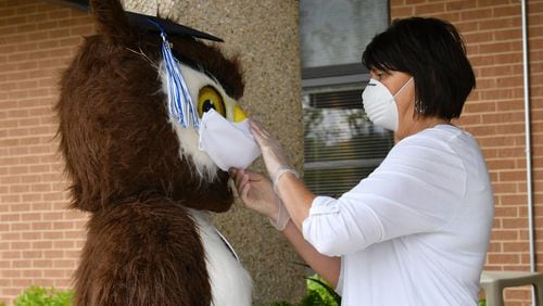 Petra Ordini (right), with office of student services, adjusts a face mask of Gwinnett Online Campus mascot Dr. Whooo, performed by Shannon Williams, as they wait for students picking up their caps and gowns last year outside the main door of Gwinnett Online Campus in Lawrenceville in 2020 .Hyosub Shin/Hyosub.Shin@ajc.com