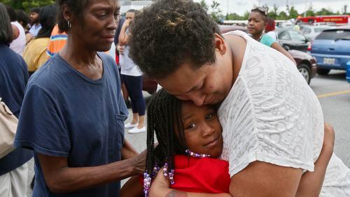 In 2013, A'Reunia Johnson, 9, gets a hug from her mother, Lecretia White, and her grandmother, Sheriza Ellis, after a gunman entered the Ronald E. McNair Discovery Learning Academy in DeKalb County and fired six rounds in a front office before surrendering to police. (Bob Andres / AJC file photo)
