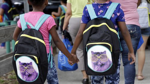 FILE - In this Aug. 15, 2015 file photo, children hold hands as they walk with their new book bags. They received the free bags as part of an annual back to school event also offering free health screenings, and free food distribution. The lazy days of summer are ending for millions of children as they grab their backpacks, pencils and notebooks and return to the classroom for a new school year. No more staying up late during the week. Farewell to sleeping in. And, hello homework! (AP Photo/Lynne Sladky, File)