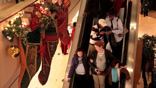 hoppers go down an escalator next to holiday decorations during a busy holiday shopping evening at Perimeter Mall.