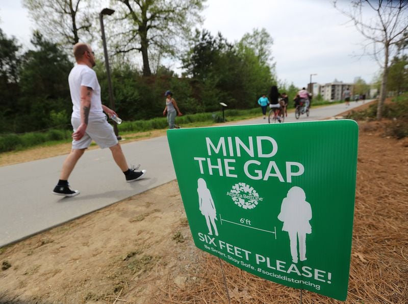A sign encourages those using the Atlanta Beltline trail to maintain six feet of distance on Sunday. Curtis Compton / ccompton@ajc.com