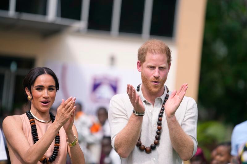 Prince Harry and Meghan gesture as they visit children at the Lights Academy in Abuja, Nigeria, Friday, May 10, 2024. Prince Harry and his wife Meghan have arrived in Nigeria to champion the Invictus Games, which he founded to aid the rehabilitation of wounded and sick servicemembers and veterans. (AP Photo/Sunday Alamba)