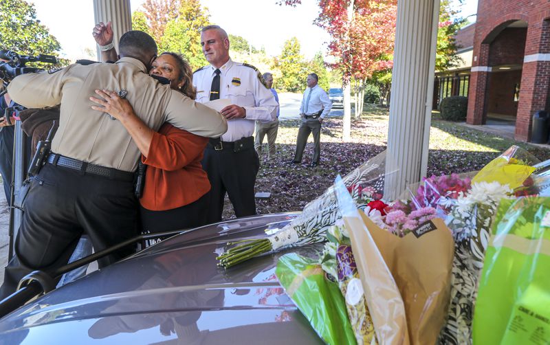Henry County Chairperson, Carlotta Harrell hugs Henry County Sheriff Reginald Scandrett (left) as Henry County Police Chief, Mark Amerman (right) looks on before the police cruiser belonging to fallen Officer Paramhans Desai. Henry County police held a press conference on Tuesday, Nov. 9, 2021, to update the public in regards to the death of Paramhans Desai. Funeral arrangements for Desai were pending Tuesday. (John Spink / John.Spink@ajc.com)



