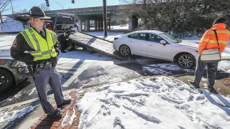 GSP trooper S. Stone (left) waits on a car to be towed from the scene after James May (right) skidded on the ice on Joseph E. Lowery Blvd. striking a concrete sewer on the I-20 entrance ramp and breaking his car’s axle. No one was hurt. JOHN SPINK/JSPINK@AJC.COM